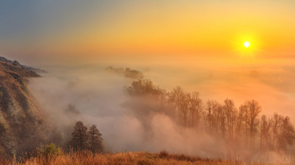 Autumn sunrise landscape - view of a river valley covered with fog in the light of the sunrays, the northeast of Ukraine