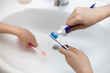 children squeeze paste onto a toothbrush near the sink