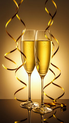Two elegant perfect glasses filled with fizzy drink or sparkling champagne with golden streamers of serpentine on golden background. Christmas, New Year, anniversary, celebration.