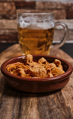 Torreznos and a beer jar on a wooden table. Spanish typical food, fried pork bacon. Appetizer.