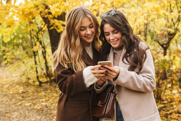 Two cheerful young pretty girls wearing coats walking together