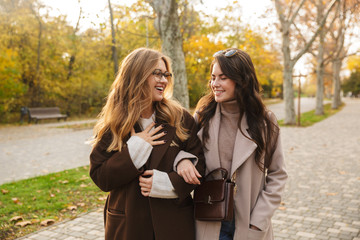 Two cheerful young pretty girls wearing coats walking together