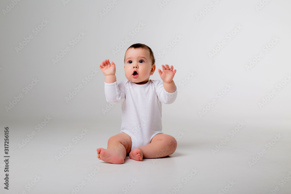 Wall mural baby boy 9 months in a white bodysuit sitting on a white background, space for text