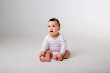 baby boy 9 months in a white bodysuit sitting on a white background, space for text