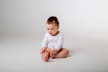 baby boy 9 months in a white bodysuit sitting on a white background, space for text