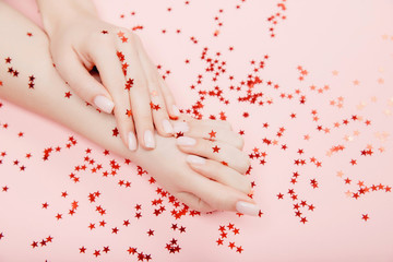 Obraz na płótnie Canvas Stylish trendy nail young woman hands pink manicure on background with red star confetti, top view. Concept skin care spa