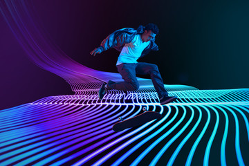 Caucasian young skateboarder riding on dark neon lighted line background. Training in action and...