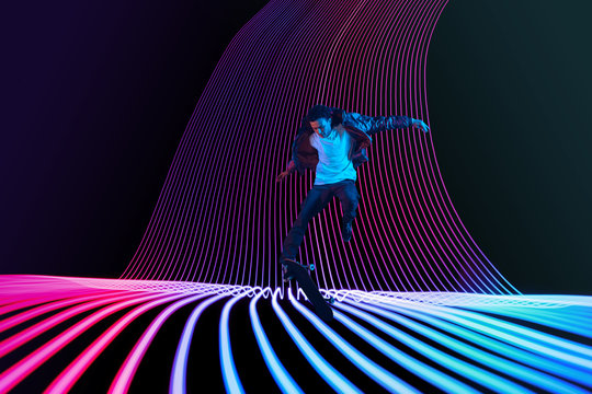 Caucasian young skateboarder riding on dark neon lighted line background. Training in action and motion on colorful waves. Concept of hobby, healthy lifestyle, youth, action, movement, modern style.