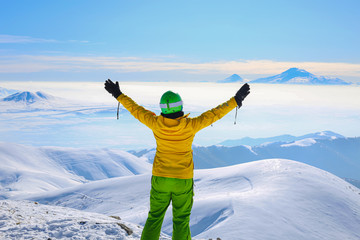 Happy woman in yellow ski jacket standing with hands up on the pick of mountain Tegenis. View of Ararat mountain.