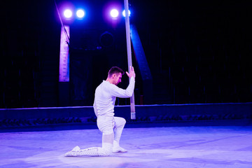 Fototapeta na wymiar side view of acrobat standing on knee near metallic pole