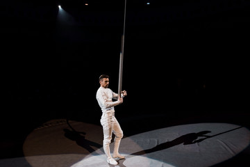 handsome acrobat standing near metallic pole in circus