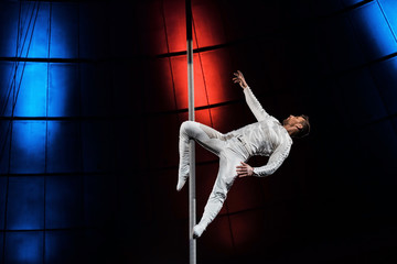 side view of strong acrobat holding metallic pole with leg while performing in circus