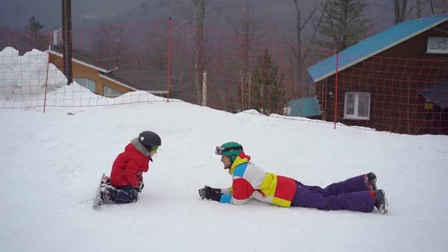 A young man and his little son have fun on a ski slope in a mountain resort activities park. Winter holidays concept. SLowmotion shot.