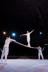 acrobats supporting man with outstretched hands walking on metallic pole in circus © LIGHTFIELD STUDIOS