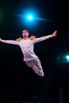 Handsome Air Acrobat With Outstretched Hands Flying In Arena Of Circus