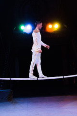 Fototapeta na wymiar side view of handsome gymnast in costume balancing while walking on pole in arena of circus