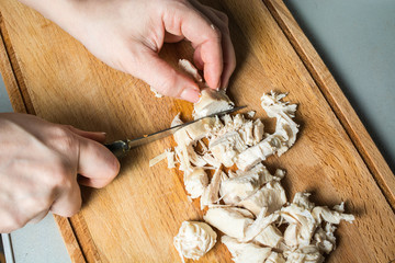 Tender hands of the girl cut with knife boiled chicken breast for salad on wooden board.