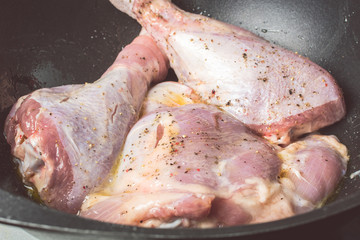Delicate raw turkey legs sprinkled with salt and pepper in large cauldron for roasting in oven.
