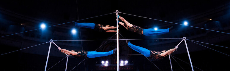 panoramic shot of four gymnasts performing on horizontal bars in circus
