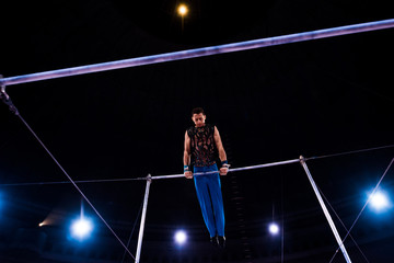Fototapeta na wymiar low angle view of athletic gymnast performing on horizontal bars in arena of circus