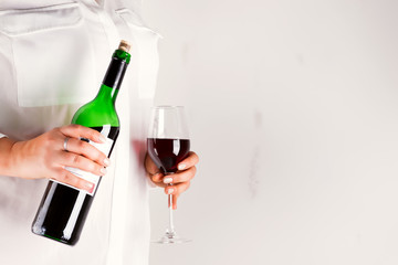 The woman holds glass with red wine and wine bottle on gray background with copy space
