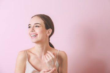 Beautiful young woman applying cream on her hand against color background