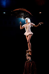 attractive woman with umbrella performing while standing on hat of man in circus © LIGHTFIELD STUDIOS