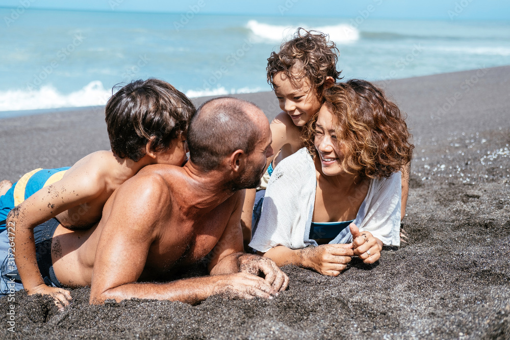 Wall mural Mixed race family lying and relaxing at the beach on beautiful summer day