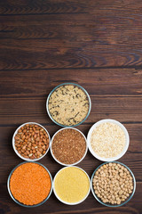 Obraz na płótnie Canvas grains red lentils, basmati rice, buckwheat, chickpeas, millet in plates. organic healthy cereals. on a wooden background. natural vegetarian vegetable protein . the view from the top. vertical frame
