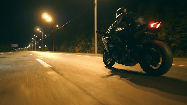 Man riding fast on modern sport motorbike at nighty city street. Motorcyclist racing his motorcycle on empty road. Guy driving bike at dusk. Concept of freedom and adventure. Low angle of view Closeup