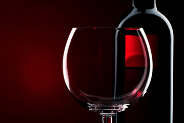 Naklejka na ściany i meble Empty wine glass for red wine and bottle, red black background, selective focus