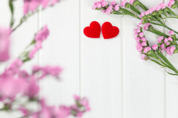 valentines day card with two red hearts and pink flower on white wooden