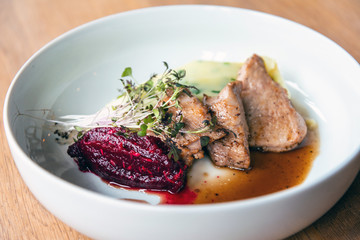 Delicious roasted pork filet cooked with smashed potatoes and smashed beetroots served in white plate.