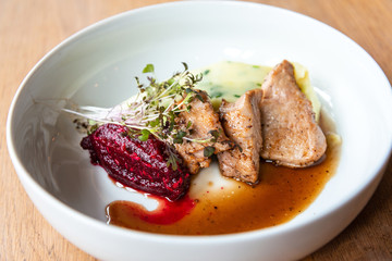 Delicious roasted pork filet cooked with smashed potatoes and smashed beetroots served in white plate.