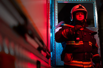 Firefighter male with hammer on his shoulder standing near fire engine.
