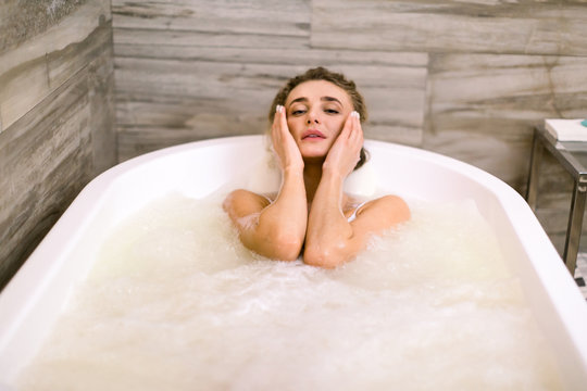 Close-up portrait of a young woman relaxing in the bathtub, getting hydromassage, touching face