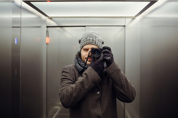 Male photographer taking a self picture in an elevator. Mirror selfie portrait, learning photography and analog film look concept.