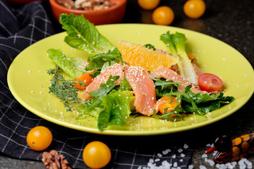 Cold salmon salad with green leaves, cucumber, avocado, lime and tomato on black stone background. Top view with copy space. Rustic style.