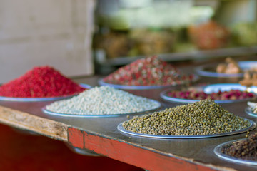 Spices of all kinds and colors, mixed black and white red pepper, colored pepper, in metal bowls. Against a blurry background. Mahane Yehuda Market, Israel.