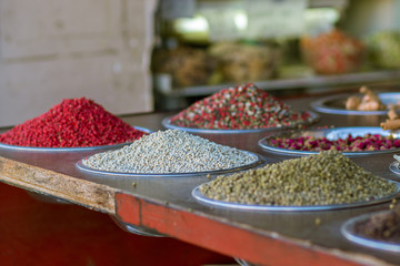 Spices of all kinds and colors, mixed black and white red pepper, colored pepper, in metal bowls. Against a blurry background. Mahane Yehuda Market, Israel.
