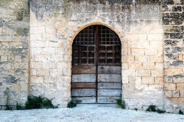 Fototapeta na wymiar Wooden door with bars and an arch in a stone wall. Monopoli, Italy.