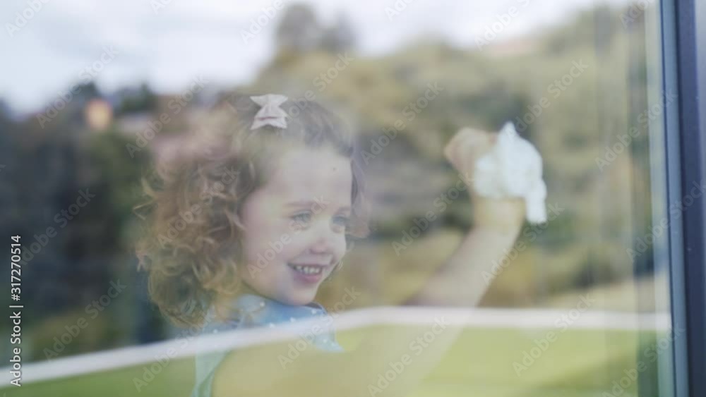 Wall mural cute small girl helping with housework indoors at home, cleaning window.