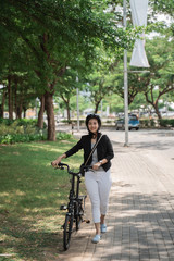 smiling working woman walks on her folding bike through the park when she gets home from work