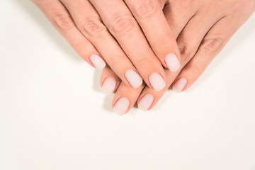 Closeup top view color photography of two beautiful female hands with modern trendy pastel natural manicure naildesign covered with finish mat top without glance. 