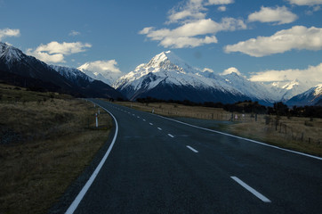 Snow covered Mount Cook with road in the foreground amd blue sky and white clouds, South Island, New Zealand
