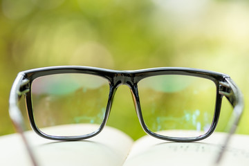 Book and eye glasses on wooden table with abstract green nature blur background. Reading and education concept