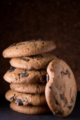 Cookies with pieces of chocolate laid out on a table on a dark background