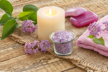 Fototapeta na wymiar Towel, soap, candle and lilac flowers on wooden background.