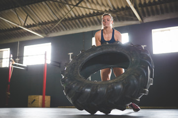 Obraz na płótnie Canvas Female fitness model doing cross fit exercise with a massive tyre in a gym