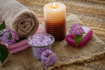 Obraz na płótnie Canvas Towels, soap, candle and lilac flowers on wooden background.